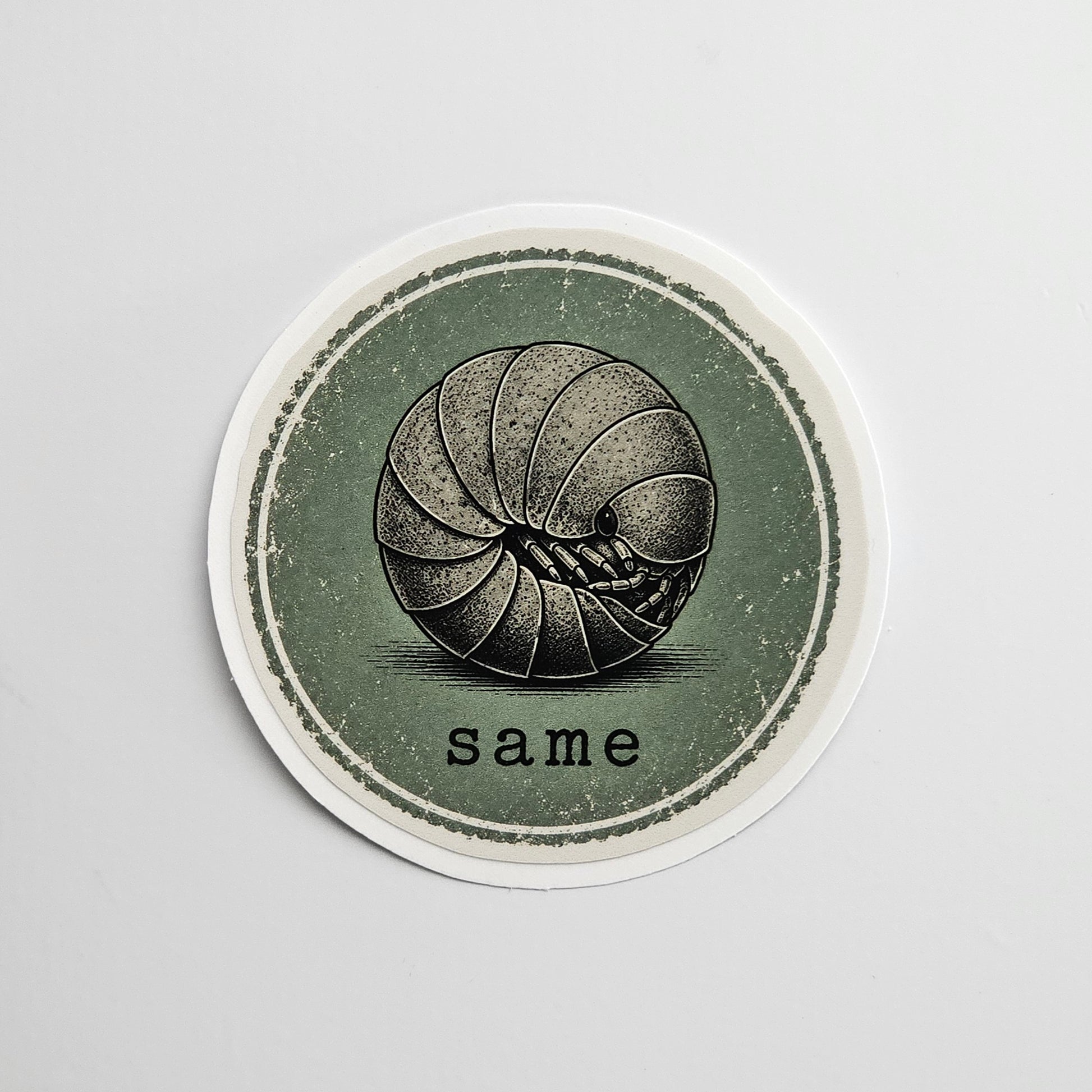 Circular sticker with a black and white roly poly illustration of a ball and the word 'same' on a gray background
